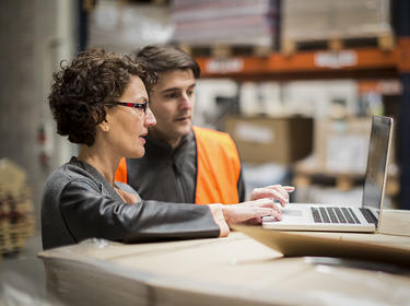 Two team members colloborate in a warehouse while looking at a laptop